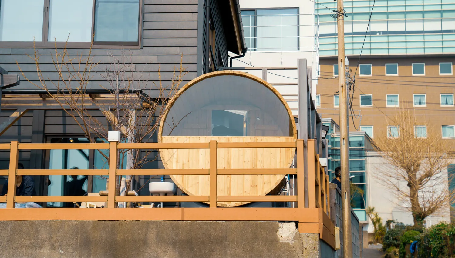 住宅のバルコニーに設置された木製バレルサウナ。丸窓から自然光が差し込む屋外サウナの外観